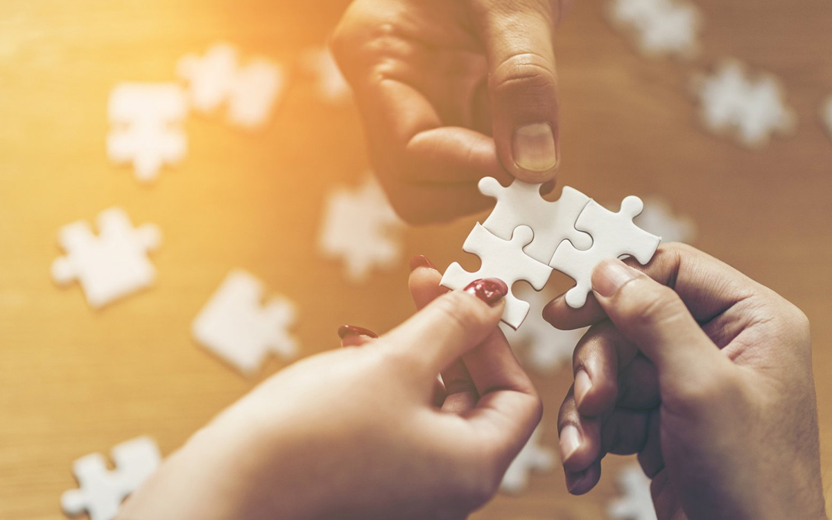 multiple hands holding puzzle pieces together