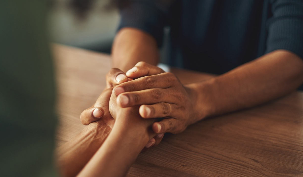 A closeup of two people holding hands while sitting across from each other at a table.